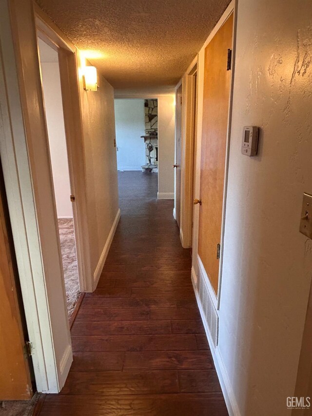 hall with a textured ceiling and dark wood-type flooring