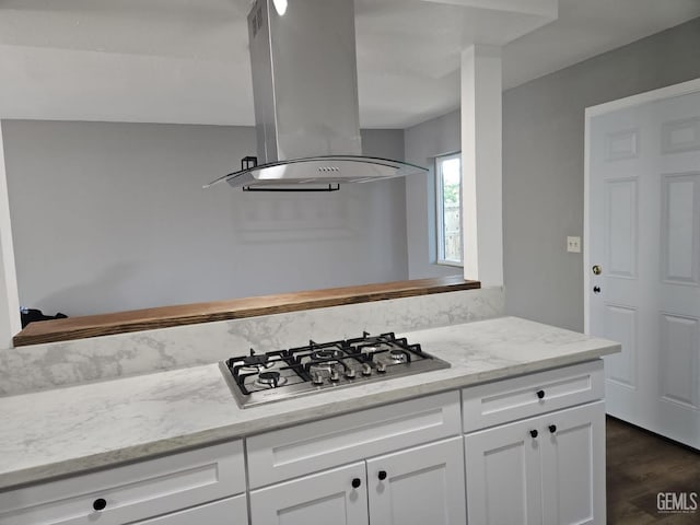 kitchen featuring light stone counters, island exhaust hood, stainless steel gas stovetop, white cabinetry, and dark hardwood / wood-style floors