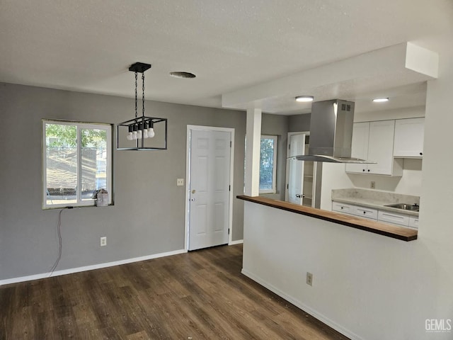 kitchen featuring dark wood-type flooring, white cabinets, island range hood, pendant lighting, and sink