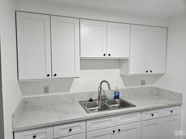 kitchen featuring white cabinetry, sink, and light stone counters