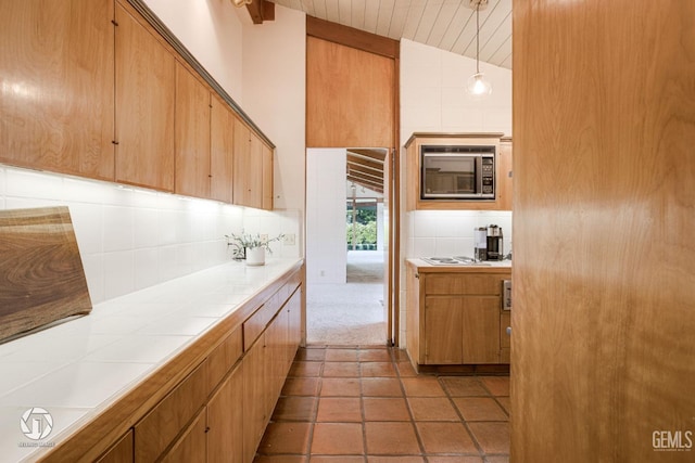 kitchen featuring tasteful backsplash, built in microwave, pendant lighting, tile counters, and lofted ceiling