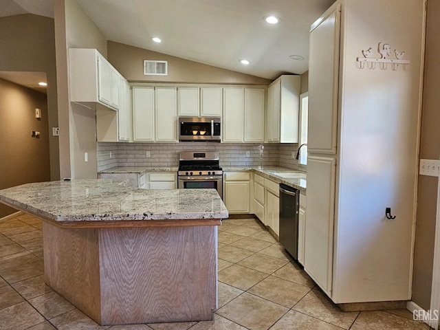 kitchen with sink, vaulted ceiling, light stone counters, and appliances with stainless steel finishes