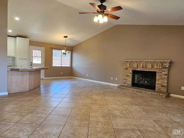 unfurnished living room featuring lofted ceiling, a brick fireplace, ceiling fan with notable chandelier, and light tile patterned floors