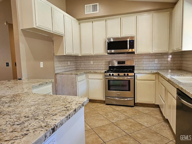 kitchen featuring light stone countertops, appliances with stainless steel finishes, light tile patterned flooring, and backsplash