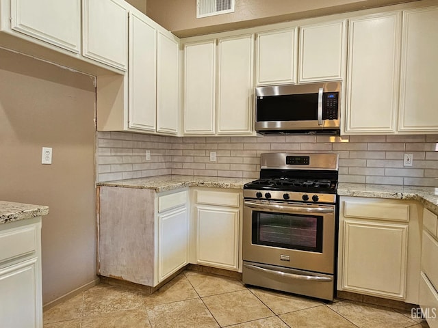 kitchen featuring light stone countertops, cream cabinets, stainless steel appliances, light tile patterned floors, and backsplash