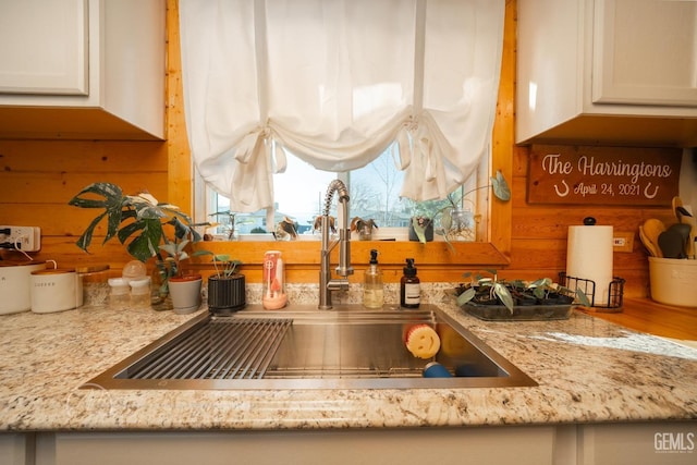 details with white cabinets, light stone countertops, wood walls, and sink