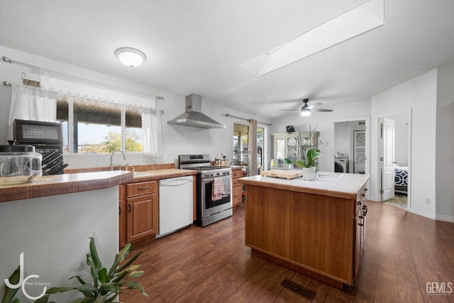 kitchen featuring a skylight, gas stove, a sink, dishwasher, and wall chimney exhaust hood