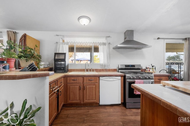 kitchen featuring dishwasher, dark wood-style floors, stainless steel range with gas stovetop, wall chimney range hood, and a sink