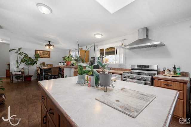 kitchen with light countertops, stainless steel range with gas cooktop, brown cabinets, wall chimney exhaust hood, and dark wood finished floors