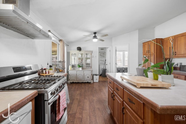 kitchen with dark wood-type flooring, wall chimney exhaust hood, brown cabinetry, plenty of natural light, and stainless steel range with gas stovetop