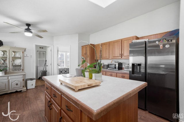 kitchen with stainless steel appliances, a kitchen island, light countertops, brown cabinets, and dark wood finished floors