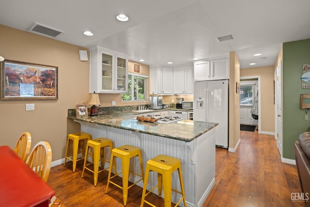 kitchen featuring kitchen peninsula, a kitchen breakfast bar, white cabinets, and white fridge with ice dispenser