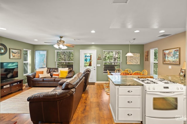 kitchen featuring white gas range, dark stone counters, white cabinets, light hardwood / wood-style floors, and hanging light fixtures