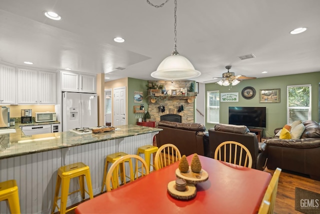 dining space featuring ceiling fan, dark hardwood / wood-style floors, and a stone fireplace