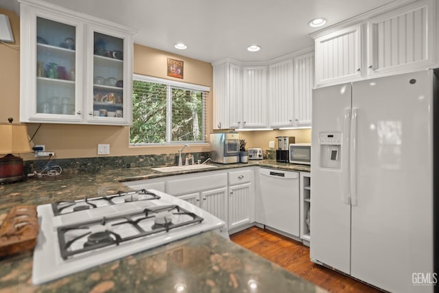 kitchen featuring white appliances, dark wood-type flooring, sink, dark stone countertops, and white cabinetry