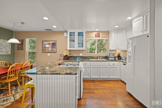 kitchen featuring kitchen peninsula, a breakfast bar, white appliances, white cabinetry, and plenty of natural light