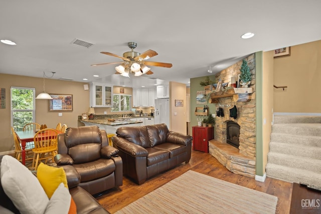 living room featuring dark hardwood / wood-style floors, ceiling fan, and a stone fireplace