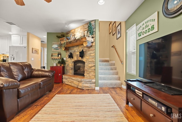 living room with hardwood / wood-style flooring, a stone fireplace, and ceiling fan