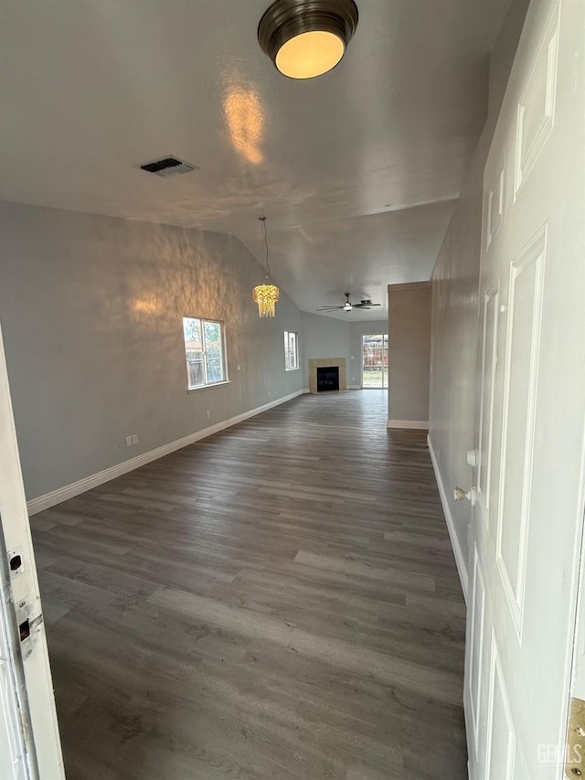 unfurnished dining area with ceiling fan, a fireplace, dark wood finished floors, baseboards, and vaulted ceiling