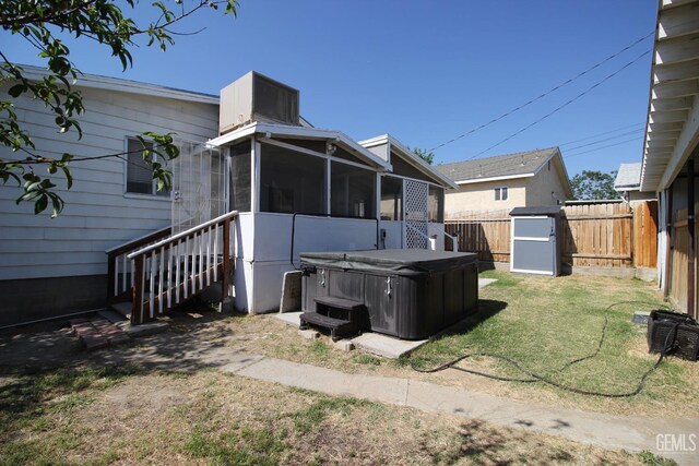 back of property with a sunroom, a hot tub, a fenced backyard, a storage unit, and a yard