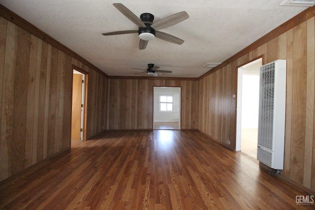 spare room featuring a heating unit, wood walls, ceiling fan, dark wood-style floors, and a textured ceiling