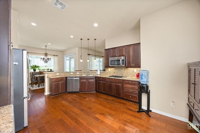 kitchen with a peninsula, appliances with stainless steel finishes, pendant lighting, and a sink