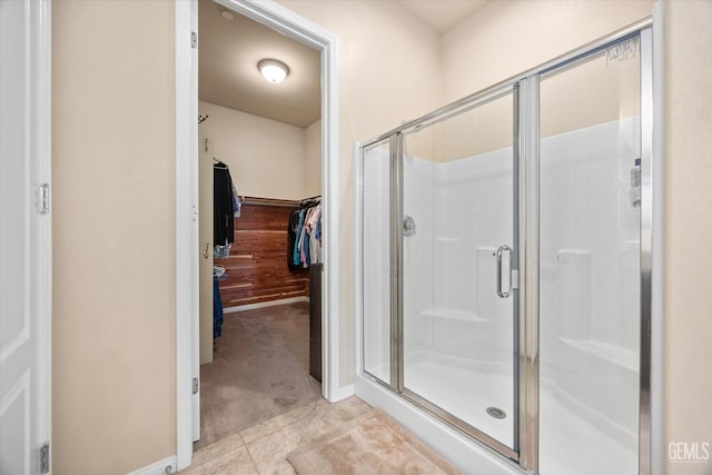 full bathroom with a stall shower, a walk in closet, tile patterned flooring, and baseboards