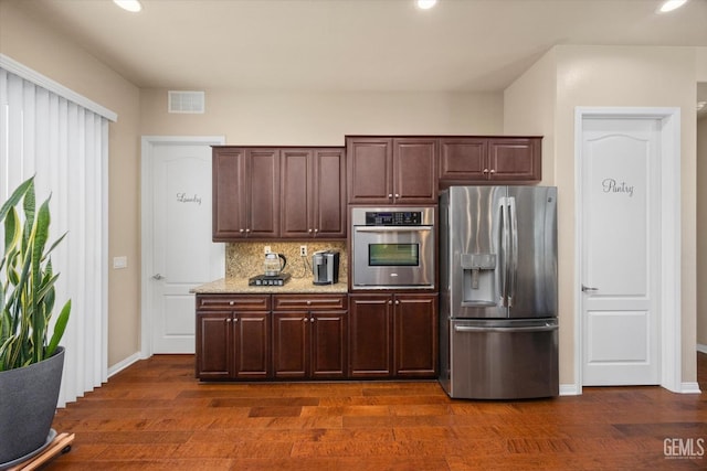 kitchen with visible vents, decorative backsplash, dark wood-style flooring, light stone countertops, and stainless steel appliances