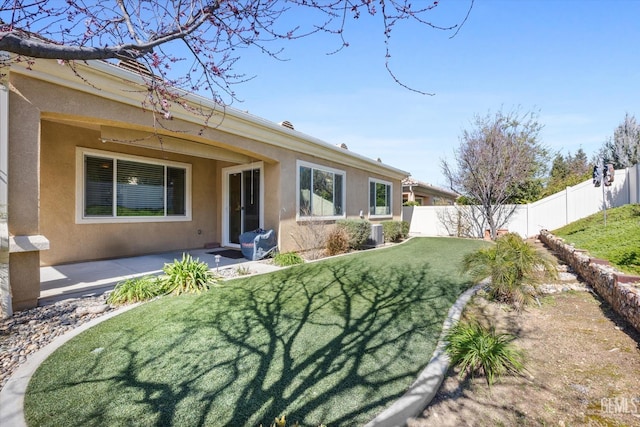 rear view of house with fence, a lawn, central AC unit, and stucco siding