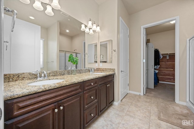 full bathroom featuring a sink, baseboards, a spacious closet, a shower stall, and double vanity