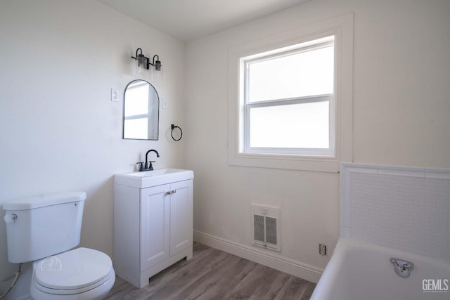 bathroom with visible vents, vanity, wood finished floors, toilet, and a bathing tub