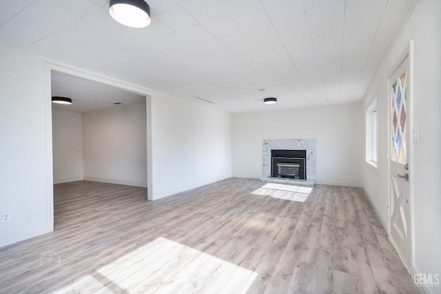 unfurnished living room featuring baseboards, visible vents, a high end fireplace, and light wood-style floors