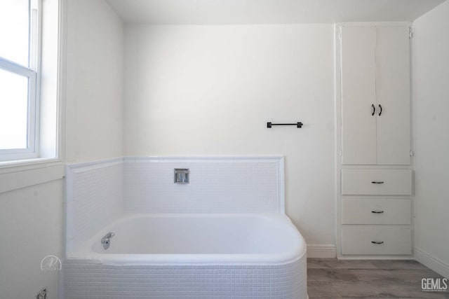 bathroom with baseboards, wood finished floors, and a bath
