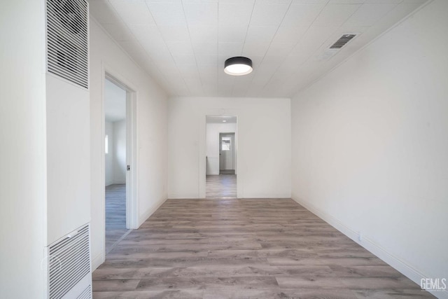 hallway with a heating unit, visible vents, and wood finished floors