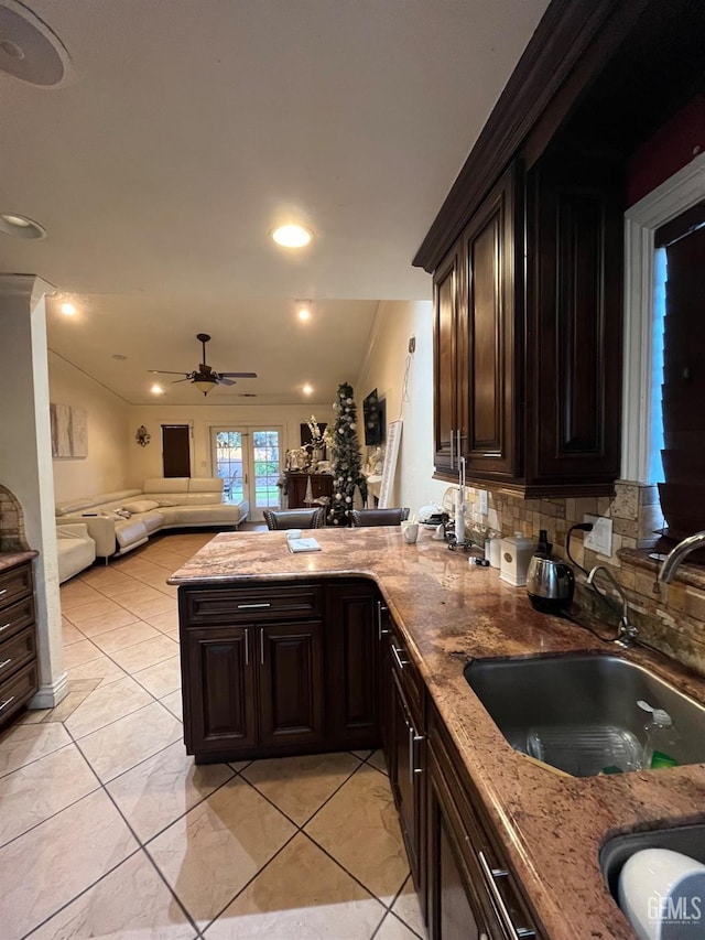 kitchen featuring light stone countertops, a peninsula, ornamental molding, a sink, and open floor plan