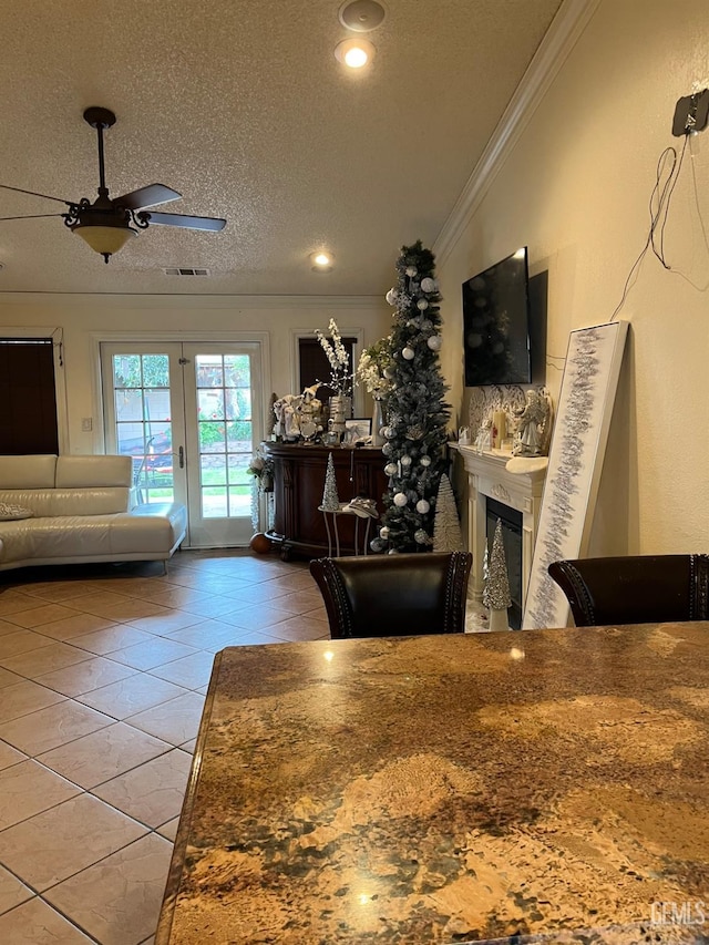 tiled living room with a ceiling fan, a textured ceiling, a glass covered fireplace, french doors, and crown molding