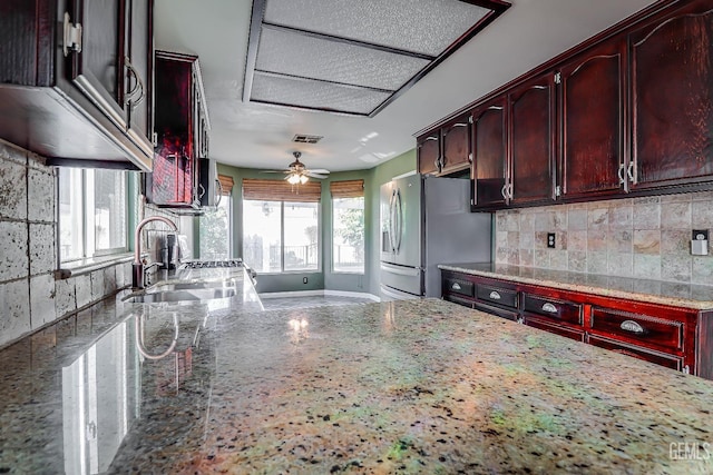 kitchen with stainless steel refrigerator with ice dispenser, sink, and light stone counters