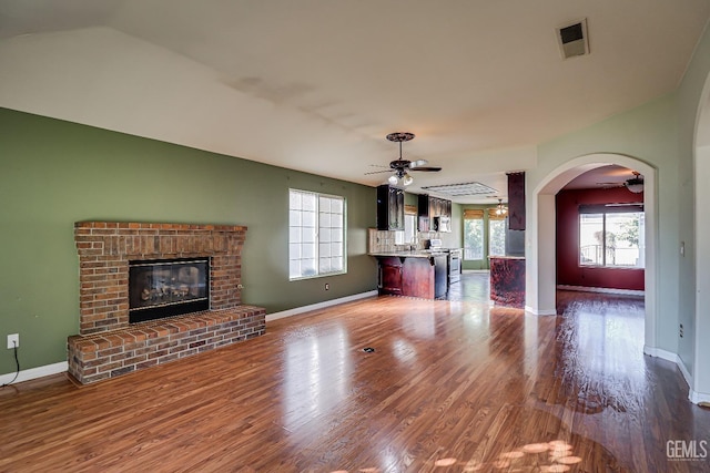 unfurnished living room featuring a healthy amount of sunlight, ceiling fan, wood-type flooring, and a brick fireplace