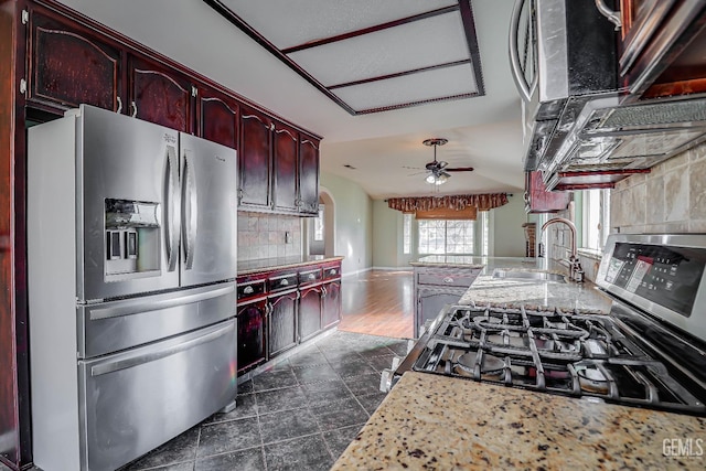 kitchen with sink, tasteful backsplash, light stone counters, appliances with stainless steel finishes, and ceiling fan