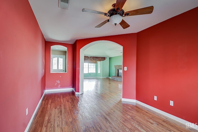 empty room with ceiling fan, a fireplace, and light hardwood / wood-style floors