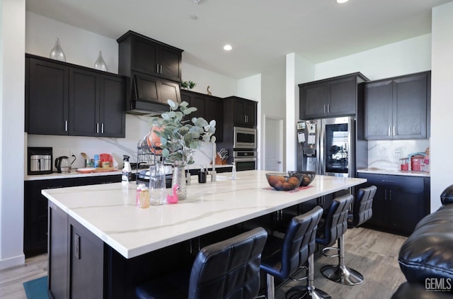 15920 Waterford St, Bakersfield, CA 93314 - kitchen featuring stainless steel appliances, a spacious island, light wood-type flooring, a kitchen breakfast bar, and light stone counters