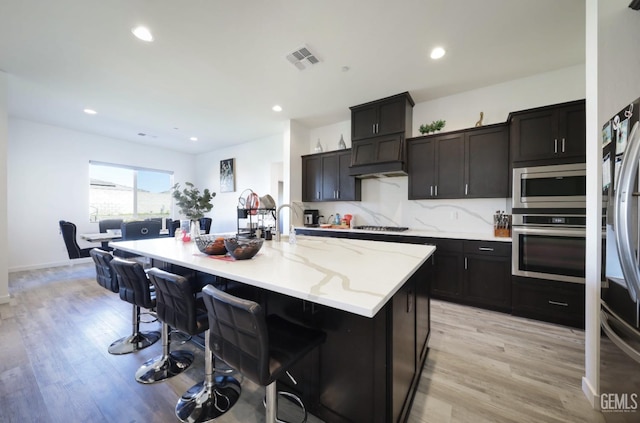 15920 Waterford St, Bakersfield, CA 93314 - kitchen with appliances with stainless steel finishes, light wood-style flooring, a kitchen breakfast bar, light stone counters, and an island with sink