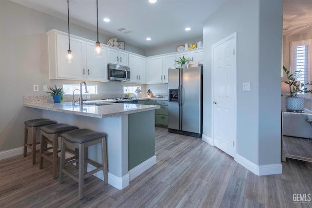 kitchen with appliances with stainless steel finishes, sink, white cabinets, hanging light fixtures, and kitchen peninsula