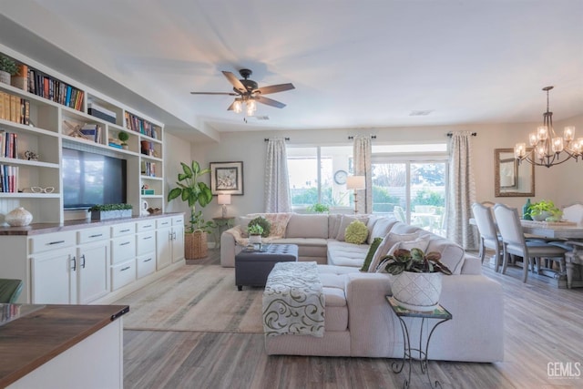 living room with ceiling fan with notable chandelier and light hardwood / wood-style flooring