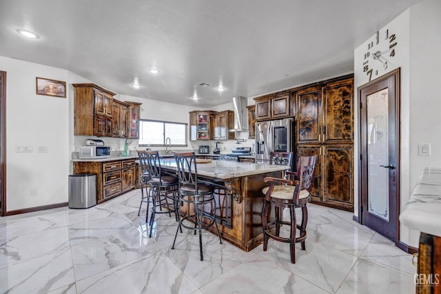 28124 Mustang Ave, Taft, CA 93268 - kitchen featuring wall chimney range hood, a breakfast bar area, light marble finish floors, appliances with stainless steel finishes, and a kitchen island