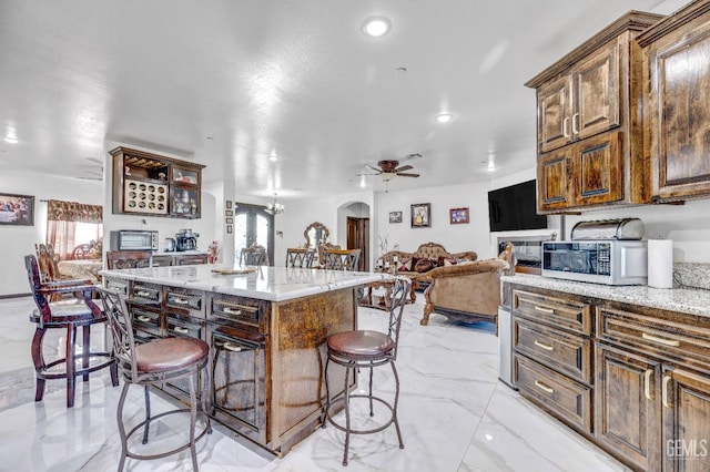 28124 Mustang Ave, Taft, CA 93268 - kitchen with white microwave, light marble finish floors, a breakfast bar area, ceiling fan, and a kitchen island