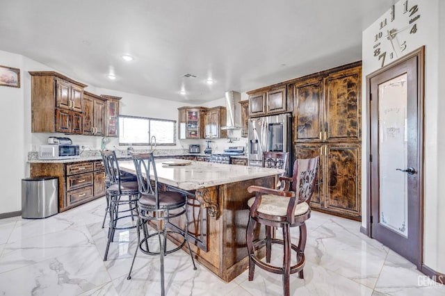 28124 Mustang Ave, Taft, CA 93268 - kitchen with appliances with stainless steel finishes, wall chimney exhaust hood, a breakfast bar area, light marble finish floors, and light stone countertops