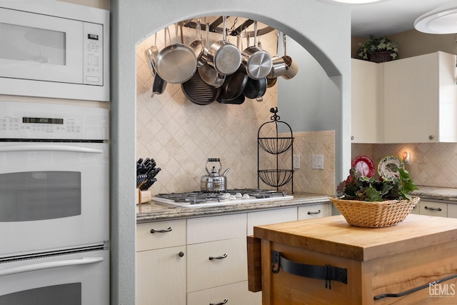 kitchen with a textured wall, white appliances, butcher block counters, white cabinets, and backsplash