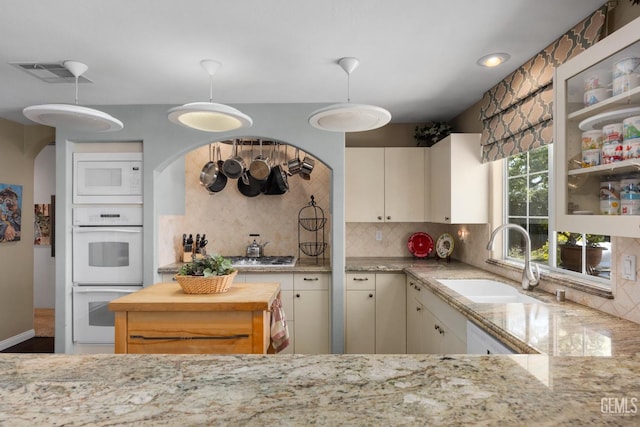 kitchen with light stone counters, white appliances, a sink, visible vents, and decorative backsplash