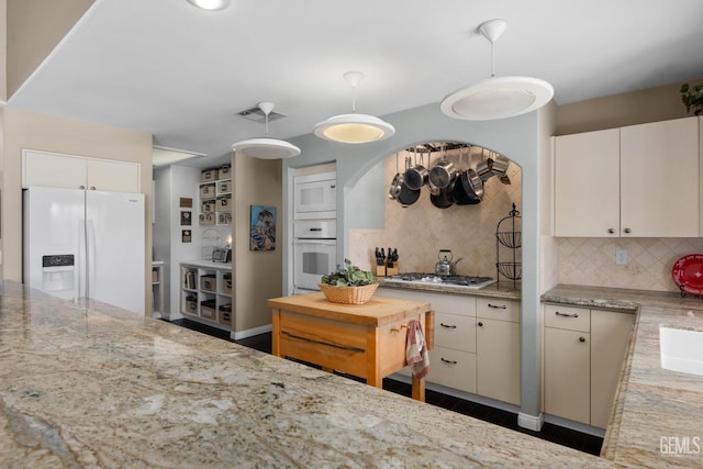 kitchen with white appliances, visible vents, backsplash, light stone countertops, and decorative light fixtures